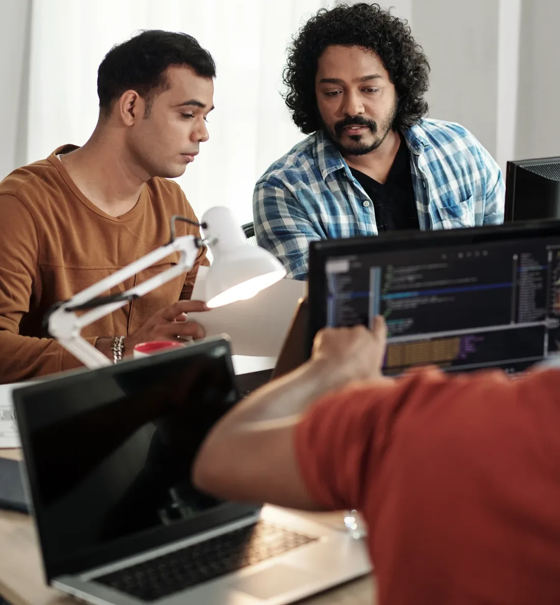 Three colleagues reviewing code together, one pointing at the screen.
